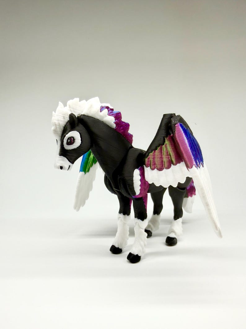 May include: A 3D-printed Pegasus figurine with a black body, white mane, and multi-colored wings. The wings feature a gradient of colors including pink, purple, blue, and green. The figurine has white legs with black hooves and a white tail.