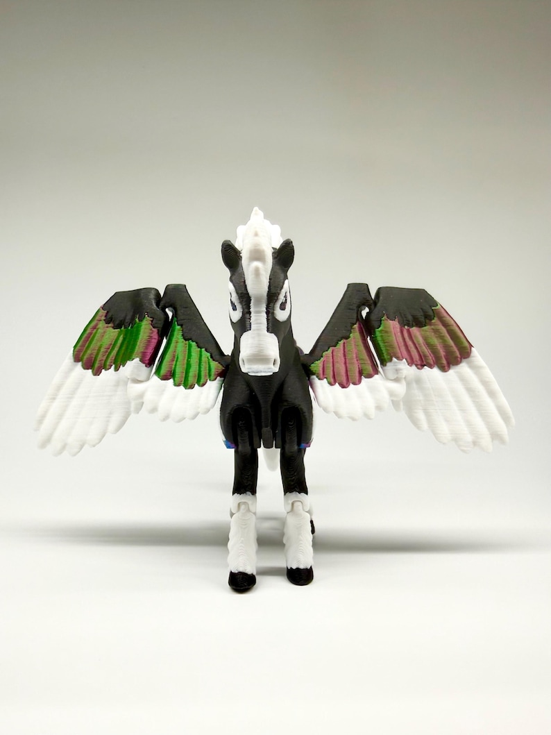 May include: A 3D-printed Pegasus figurine. The black horse has white wings with green and pink accents. The mane and lower legs are white. The figurine is standing with its wings spread.