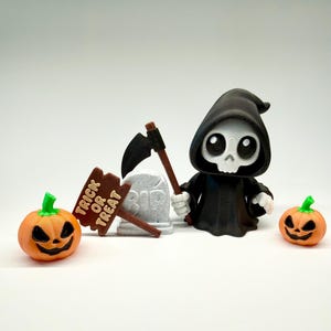 May include: A Halloween-themed display featuring a cartoon Grim Reaper figure with a scythe, two orange jack-o'-lanterns, a tombstone, and a brown sign that reads "Trick or Treat". The Reaper wears a black hooded robe.