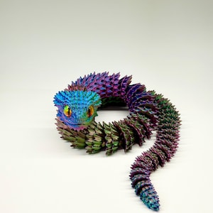 May include: A colorful, articulated snake toy with a textured, iridescent finish. The snake's head is blue, transitioning to purple and green along its body. The eyes are yellow and orange.