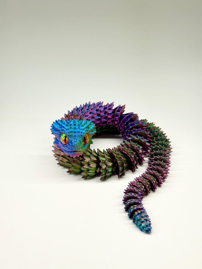May include: A colorful, articulated snake toy with a textured, iridescent finish. The snake's head is blue, transitioning to purple and green along its body. The eyes are yellow and orange.