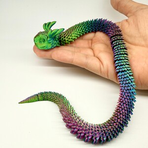 May include: A colorful, articulated dragon toy, approximately 13.8 inches (35cm) long. The dragon features a green head with large ears and a body that transitions from green to purple. The text "Length 13.8in(35cm) Colorful 2" is visible.