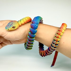 May include: A colorful, articulated snake toy with a rainbow gradient design. The snake's head is yellow and green, transitioning to blue, red, and orange along its body. The toy is wrapped around a wrist.