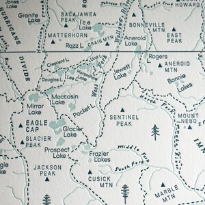 May include: A detailed map featuring mountain ranges, lakes, and rivers. The map includes names like Eagle Cap, Glacier Lake, and the Wallowa River. The color palette is a soft, muted green and white, with dashed lines indicating boundaries.