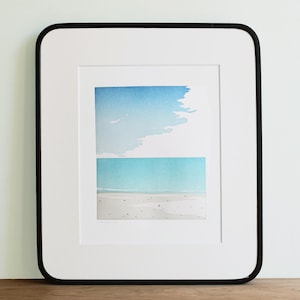 May include: A framed watercolor painting of a beach scene with a blue sky and ocean. The painting is divided into two sections, with the top section showing the sky and the bottom section showing the ocean and beach.