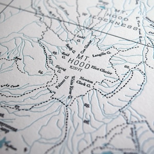Puede incluir: Un primer plano de un mapa que muestra la ubicaci&oacute;n del Monte Hood, Oreg&oacute;n. El mapa est&aacute; impreso en blanco y negro sobre un fondo blanco. La elevaci&oacute;n del Monte Hood se indica como 11.237 pies. El mapa muestra la ubicaci&oacute;n de varios glaciares, incluidos el glaciar Coe, el glaciar Eliot y el glaciar Langille.