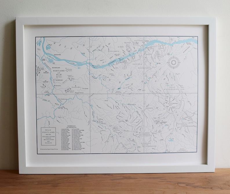 Puede incluir: Un mapa enmarcado del &aacute;rea de Wild Portland, que muestra r&iacute;os, lagos y senderos. El mapa est&aacute; impreso en azul y negro sobre un fondo blanco. El t&iacute;tulo "Wild Portland" est&aacute; impreso en negro en la parte inferior del mapa. El mapa incluye una clave con una lista de cascadas y rutas de senderismo.