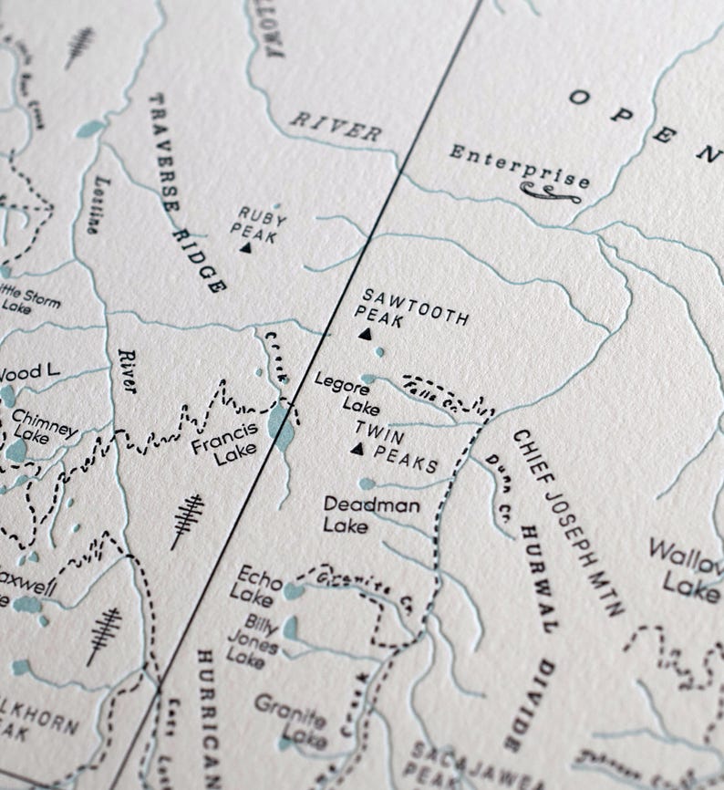 May include: Close-up of a detailed map with topographical features. The map features names like "Sawtooth Peak," "Francis Lake," and "Enterprise." The color palette is muted, with a cream background and blue-gray lines, creating a vintage aesthetic.