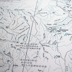 Puede incluir: Un mapa en blanco y negro de un &aacute;rea silvestre con los nombres "Salmon-Huckleberry Wilderness" y "Roaring River Wilderness" impresos en &eacute;l. El mapa muestra r&iacute;os, arroyos, monta&ntilde;as y otras caracter&iacute;sticas geogr&aacute;ficas.