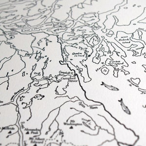 May include: A detailed black and white map print showing coastal regions, islands, and rivers. The map includes place names such as Campbell River and Quadra Island, with fish illustrations. The style is reminiscent of a nautical chart.