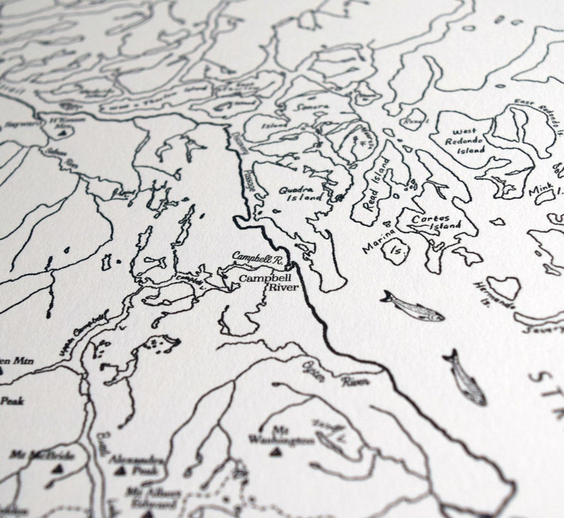 May include: A detailed black and white map print showing coastal regions, islands, and rivers. The map includes place names such as Campbell River and Quadra Island, with fish illustrations. The style is reminiscent of a nautical chart.