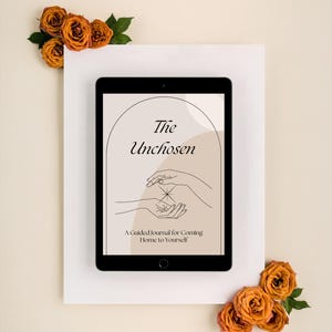 Può includere: Un tablet nero mostra il titolo "The Unchosen" con un disegno a tratto di mani e il testo "A Guided Journal for Coming Home to Yourself". Il tablet è su una superficie bianca, decorato con rose arancioni.