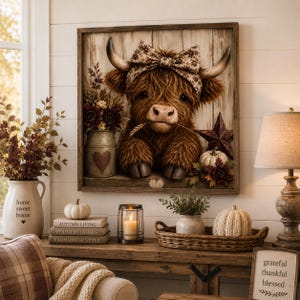 May include: A square framed wall art piece featuring a fluffy brown highland cow wearing a patterned bow between its horns. The cow holds a wheat stalk in its mouth, set against a rustic wood-plank background with a metal star and flowers.