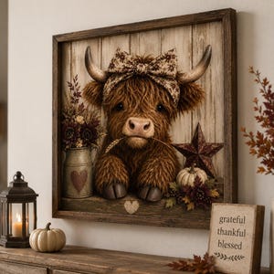 May include: A framed wall art piece featuring a fluffy brown Highland cow wearing a patterned bow between its horns. The cow holds a wheat stalk in its mouth. The scene includes a metal milk jug, a rustic star, and a small pumpkin on a wood background.