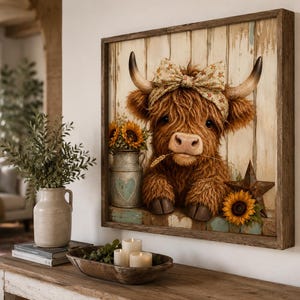 Op de afbeelding: Een vierkant ingelijst kunstwerk aan de muur met een pluizige bruine Schotse Hooglander die een hoofdband met bloemenpatroon draagt. De koe staat voor een rustieke achtergrond van witte houten planken met een metalen melkkan, zonnebloemen en een ster.