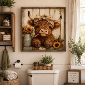 Op de afbeelding: Een vierkante wandkunstprint met een pluizige bruine Schotse Hooglander met een bloemenhoofdband, geplaatst voor een rustieke witte houten achtergrond. De koe houdt een tarwestengel in de mond naast een metalen kan met zonnebloemen.