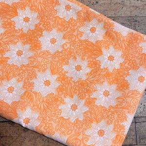 May include: Orange fabric with a white floral pattern. The fabric has a vintage look and feel.