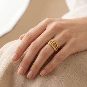 Puede incluir: Un anillo de banda de oro que presenta una serie de recortes de arco verticales repetidos alrededor de toda la circunferencia. El metal tiene un acabado pulido, creando un dise&ntilde;o calado y estructurado que rodea el dedo con un patr&oacute;n consistente.