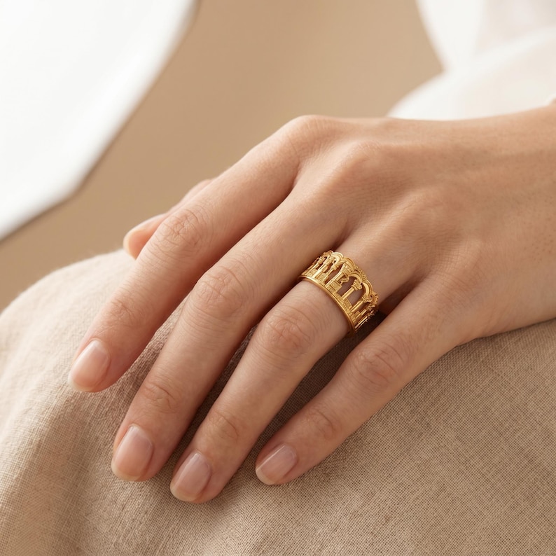 Puede incluir: Un anillo de banda de oro que presenta una serie de recortes de arco verticales repetidos alrededor de toda la circunferencia. El metal tiene un acabado pulido, creando un dise&ntilde;o calado y estructurado que rodea el dedo con un patr&oacute;n consistente.