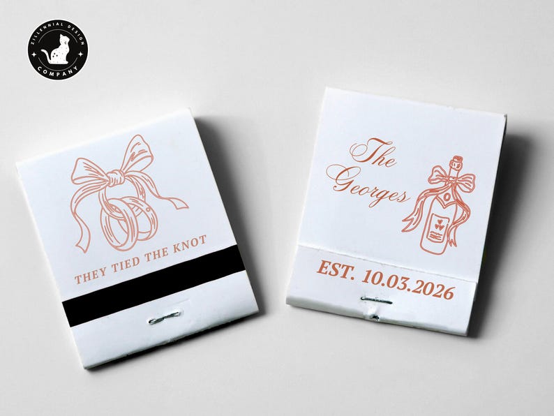 May include: Two white matchboxes with rose-gold illustrations and text. One reads "THEY TIED THE KNOT" with rings and a bow. The other says "The Georges" with a champagne bottle and bow, and "EST. 10.03.2026".