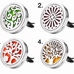 May include: Four silver car air vent diffusers with decorative designs. The diffusers have different colored inserts: green swirls, burgundy sunburst, orange tree, and gold tree. Each diffuser has a black clip for attachment.