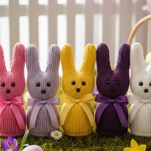 Può includere: Cinque statuette di coniglietti lavorati a maglia in rosa, lavanda, giallo, viola e bianco, ciascuna con un fiocco di nastro. I coniglietti hanno occhi a bottone neri e sono disposti su un letto di muschio verde.