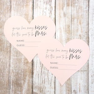May include: Two pink heart-shaped cards with the text "guess how many kisses for the soon to be Mrs." and blank lines for a name and guess.