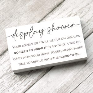 May include: White card with black text that reads "display shower" and explains that gifts do not need to be wrapped. The text also states that a tag or card with a name on it means more time to mingle with the bride-to-be.