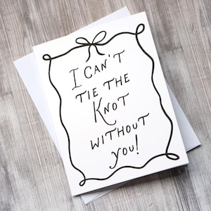 May include: A white greeting card with the handwritten phrase "I can't tie the knot without you!" in black ink. The card is framed by a black decorative border and sits on a white envelope, perfect for wedding invitations.