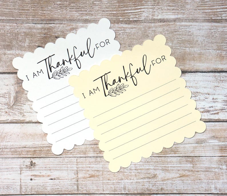 Puede incluir: Dos tarjetas con bordes festoneados, una blanca y otra amarillo p&aacute;lido, cada una con el texto impreso en negro I AM Thankful FOR sobre una peque&ntilde;a ilustraci&oacute;n de una hoja y cinco l&iacute;neas horizontales para escribir notas de gratitud.