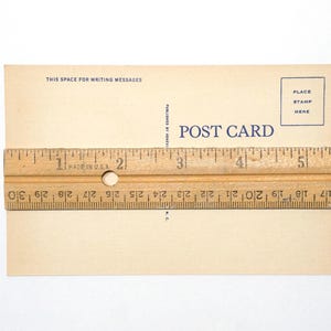 K&ouml;nnte beinhalten: Eine rechteckige beige Postkarte mit blauem Text, der POST CARD, THIS SPACE FOR WRITING MESSAGES und PLACE STAMP HERE lautet. Ein Holzlineal liegt in der Mitte und zeigt, dass die Breite der Postkarte etwa 14 cm betr&auml;gt.