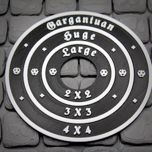 May include: A circular black and white gaming template featuring concentric rings with white text labels reading Gargantuan, Huge, and Large, followed by grid dimensions 2x2, 3x3, and 4x4. The surface has a textured finish with small white star icons.