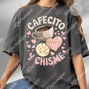 Peut inclure: T-shirt gris foncé avec l'inscription "CAFECITO CHISME" en blanc et rose. Le motif comprend une tasse de café, deux conchas et des cœurs roses. Un t-shirt décontracté pour les amateurs de café et de potins.