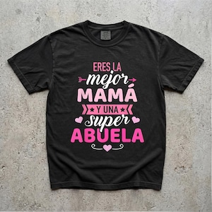 May include: Black t-shirt with the text "ERES LA MEJOR MAMA Y UNA SUPER ABUELA" in pink and white. The text is arranged in a decorative layout with arrows, stars, and hearts. A casual, comfortable style.