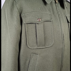 Pode incluir: Casaco verde-oliva com gola, dois bolsos no peito com bot&otilde;es e fecho frontal com z&iacute;per. O casaco tem um design cl&aacute;ssico de inspira&ccedil;&atilde;o militar.
