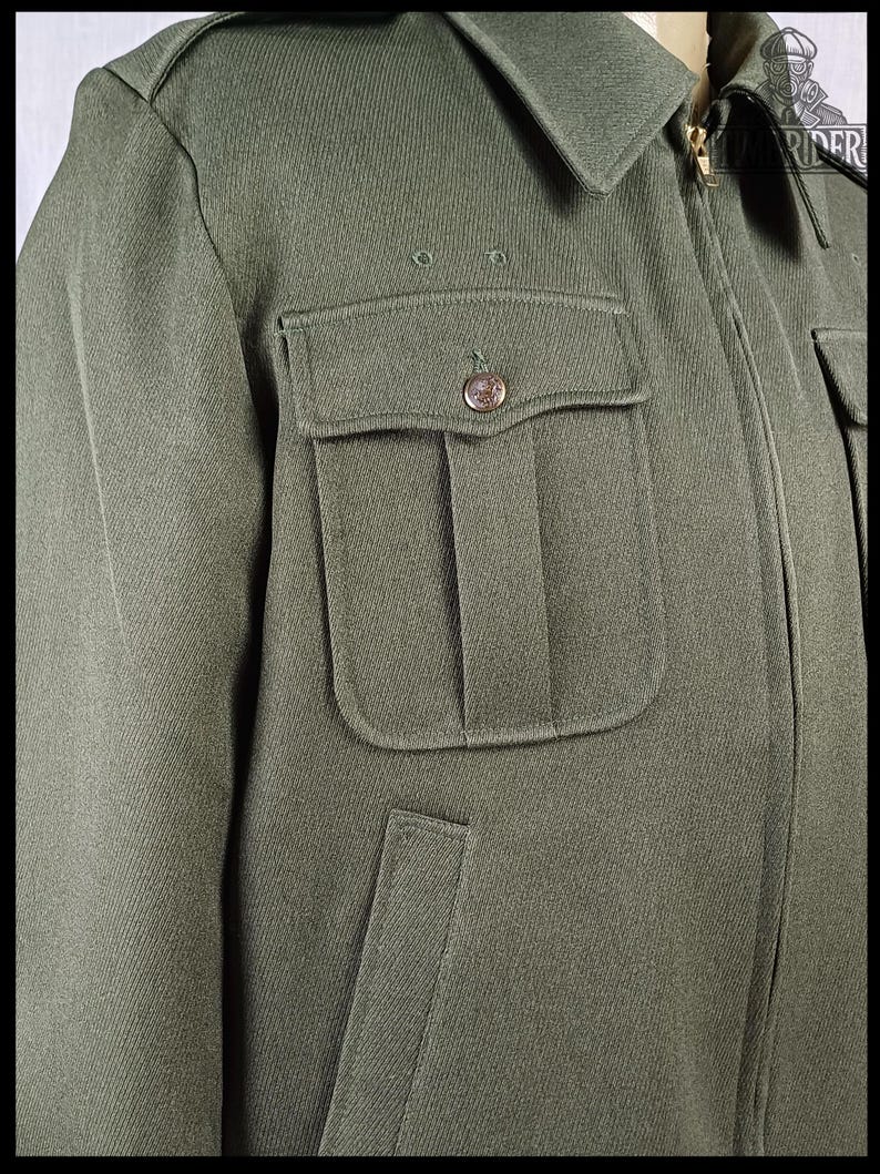 Pode incluir: Casaco verde-oliva com gola, dois bolsos no peito com bot&otilde;es e fecho frontal com z&iacute;per. O casaco tem um design cl&aacute;ssico de inspira&ccedil;&atilde;o militar.