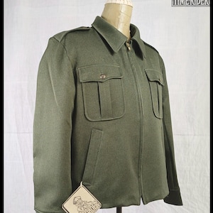 Pode incluir: Casaco verde-oliva com fecho de correr, dois bolsos no peito e dois bolsos laterais. O casaco tem gola e ombreiras. Uma etiqueta com o texto "TIMERIDER" est&aacute; presa ao casaco.