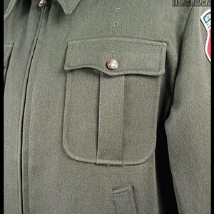 Pode incluir: Casaco verde-oliva de estilo militar com gola e z&iacute;per dourado. O casaco apresenta um bolso no peito com um bot&atilde;o decorativo e um patch na manga direita. O casaco &eacute; feito de tecido texturizado.
