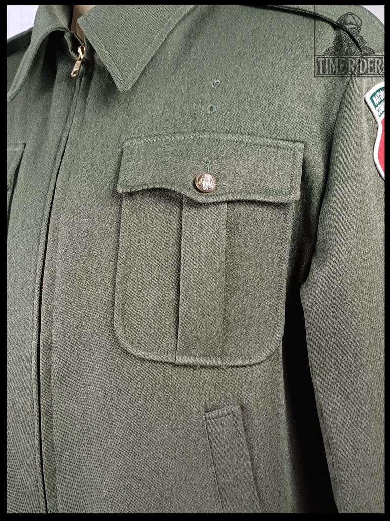 Pode incluir: Casaco verde-oliva de estilo militar com gola e z&iacute;per dourado. O casaco apresenta um bolso no peito com um bot&atilde;o decorativo e um patch na manga direita. O casaco &eacute; feito de tecido texturizado.