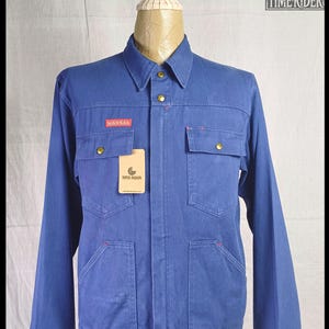 May include: A blue denim jacket with gold-colored buttons and four front pockets. The jacket has a red "KANSAS" patch and a "TIME RIDER" tag. The jacket is displayed on a mannequin.