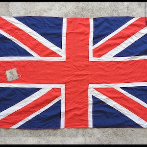 May include: A Union Jack flag, the national flag of the United Kingdom, with a red, white, and blue design. The flag has a rectangular shape and is made of fabric. A small patch with an image is attached to the flag. The text "TIME RIDER" is visible.