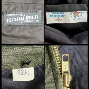 Pode incluir: Vista de perto de um casaco de uniforme verde-oliva vintage. A imagem mostra etiquetas com texto, incluindo "UNIFORMS by FECHHEIMER CINCINNATI", "PROFESSIONAL DRY CLEAN ONLY" e "42R". Um fecho de correr YKK dourado tamb&eacute;m &eacute; vis&iacute;vel.