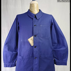 Peut inclure: Veste de travail bleue avec col, fermeture boutonnée et plusieurs poches. La veste est présentée sur un mannequin. Une étiquette avec le texte "TIME RIDER" est attachée à la veste.