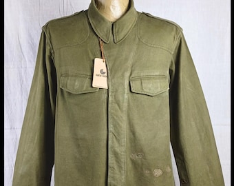 May include: A green military-style jacket with a button-up front and two large pockets. The jacket has a distressed look with some holes and faded areas. The label on the jacket reads "GANT Rugger".