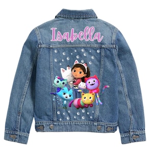 Può includere: Giacca di jeans blu con il nome "Isabella" in rosa. La parte posteriore della giacca presenta una grafica a cartoni animati colorati e strass. Ha una chiusura con bottoni e due tasche.