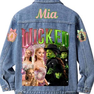 May include: A light blue denim jacket with the name "Mia" in pink script above a graphic of the musical "Wicked". The graphic includes images of the musical's characters and butterflies. Decorative patches are on the jacket.