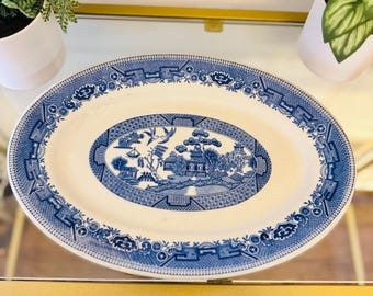 May include: Oval serving platter with a blue and white Willow pattern design. The platter features a central landscape scene surrounded by a decorative border. The dish is made of ceramic and is suitable for serving food.