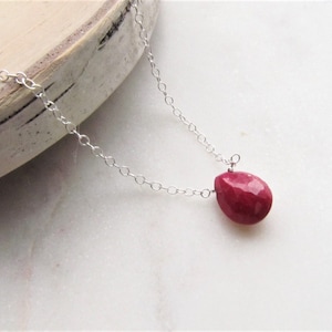 May include: A silver chain necklace with a teardrop-shaped red gemstone pendant.