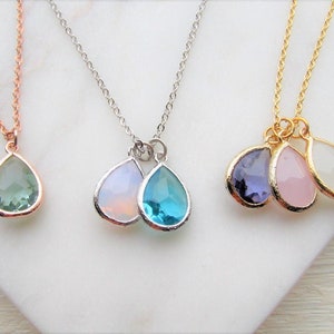 May include: Three delicate necklaces with teardrop-shaped pendants. The necklaces are made of gold, silver, and rose gold chains. The pendants are made of various colored gemstones, including green, blue, purple, pink, and white.