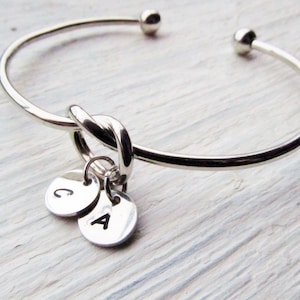 May include: Silver bangle bracelet with a knotted design and two small charms with the letters 'C' and 'A' engraved on them.